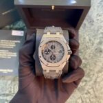 Stainless steel chronograph wristwatch held by a gloved hand, with a dark presentation box in the background.