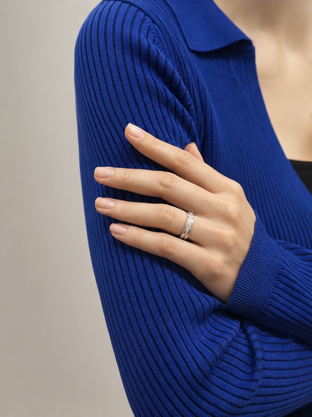Close-up of a hand wearing a silver ring on the ring finger, resting on a cobalt blue ribbed sweater sleeve.