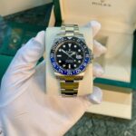 Rolex GMT‑Master II diverless watch with a black dial and blue/black 24‑hour bezel held by gloved hand, in a green Rolex box.
