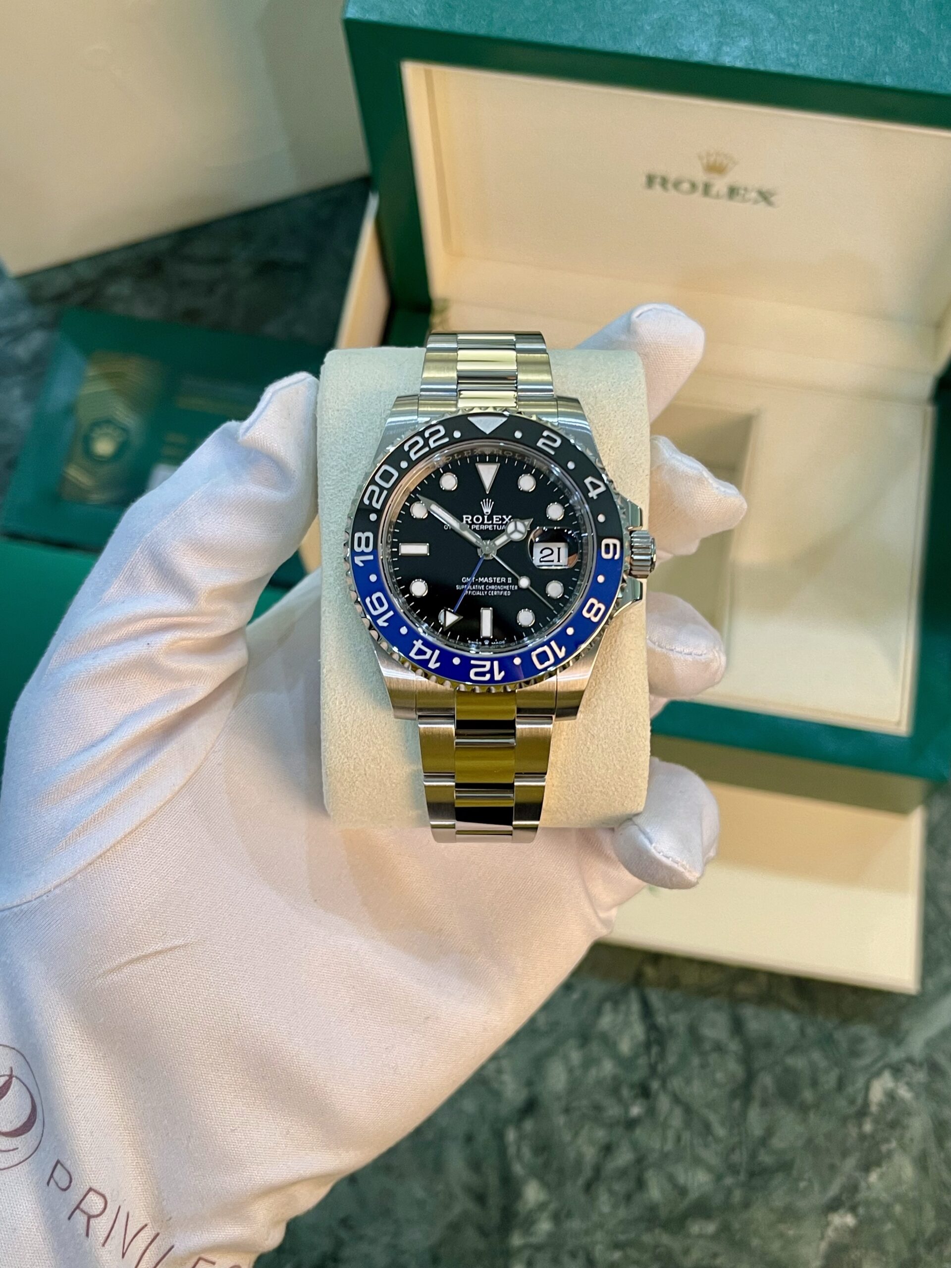 Rolex GMT‑Master II diverless watch with a black dial and blue/black 24‑hour bezel held by gloved hand, in a green Rolex box.