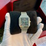 Cartier Santos stainless-steel watch with Roman numerals on a square face, displayed on a black cushion inside a red presentation box.