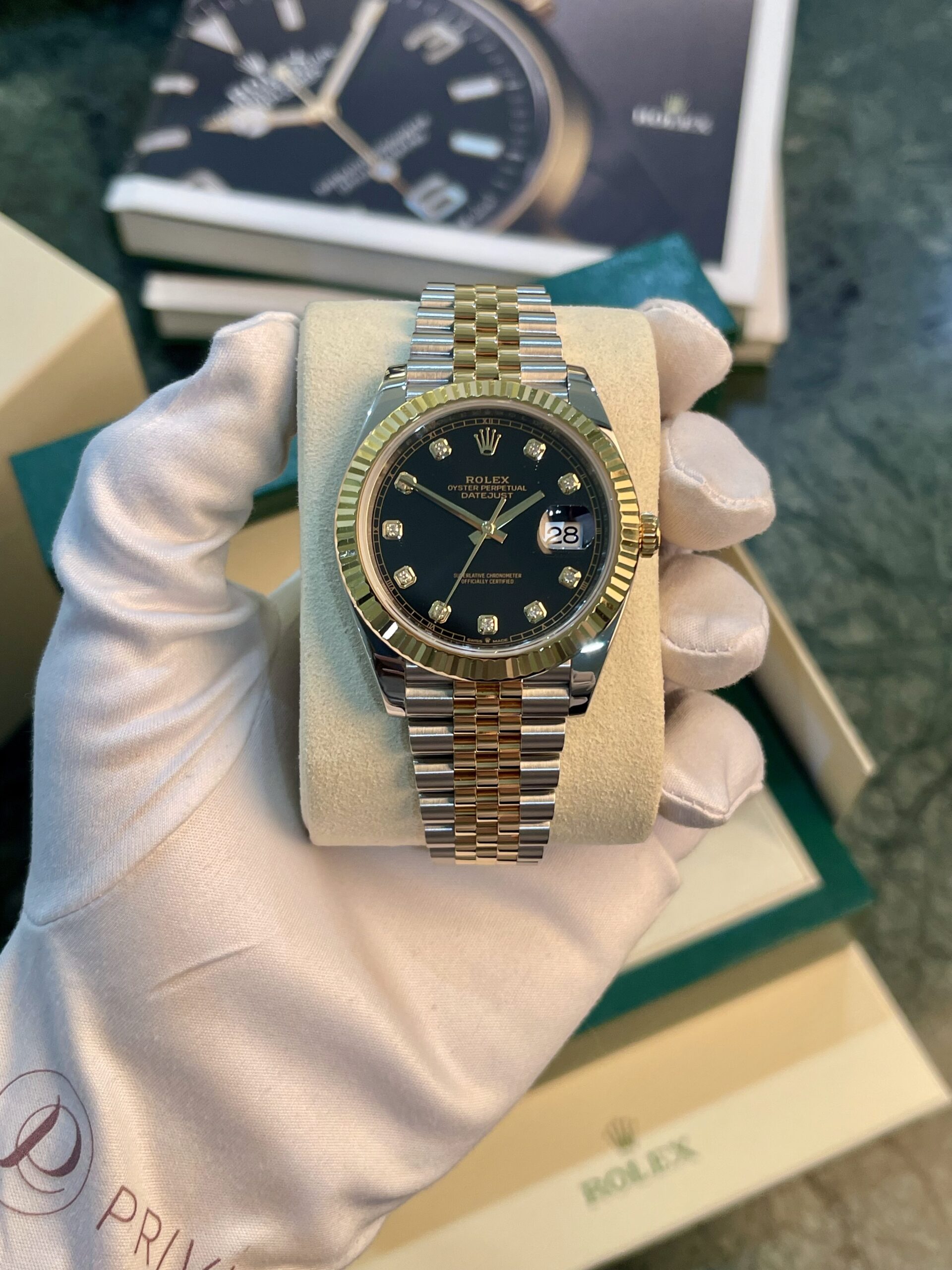 Rolex Datejust wristwatch with a two-tone gold and steel bracelet and diamond hour markers held by a gloved hand.