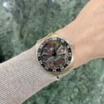 Stainless steel TAG Heuer Formula 1 watch on a wrist with a beige knit sleeve, against a green marble-like background.