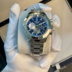 Zenith El Primero wristwatch with blue dial and silver subdials, held in a gloved hand.