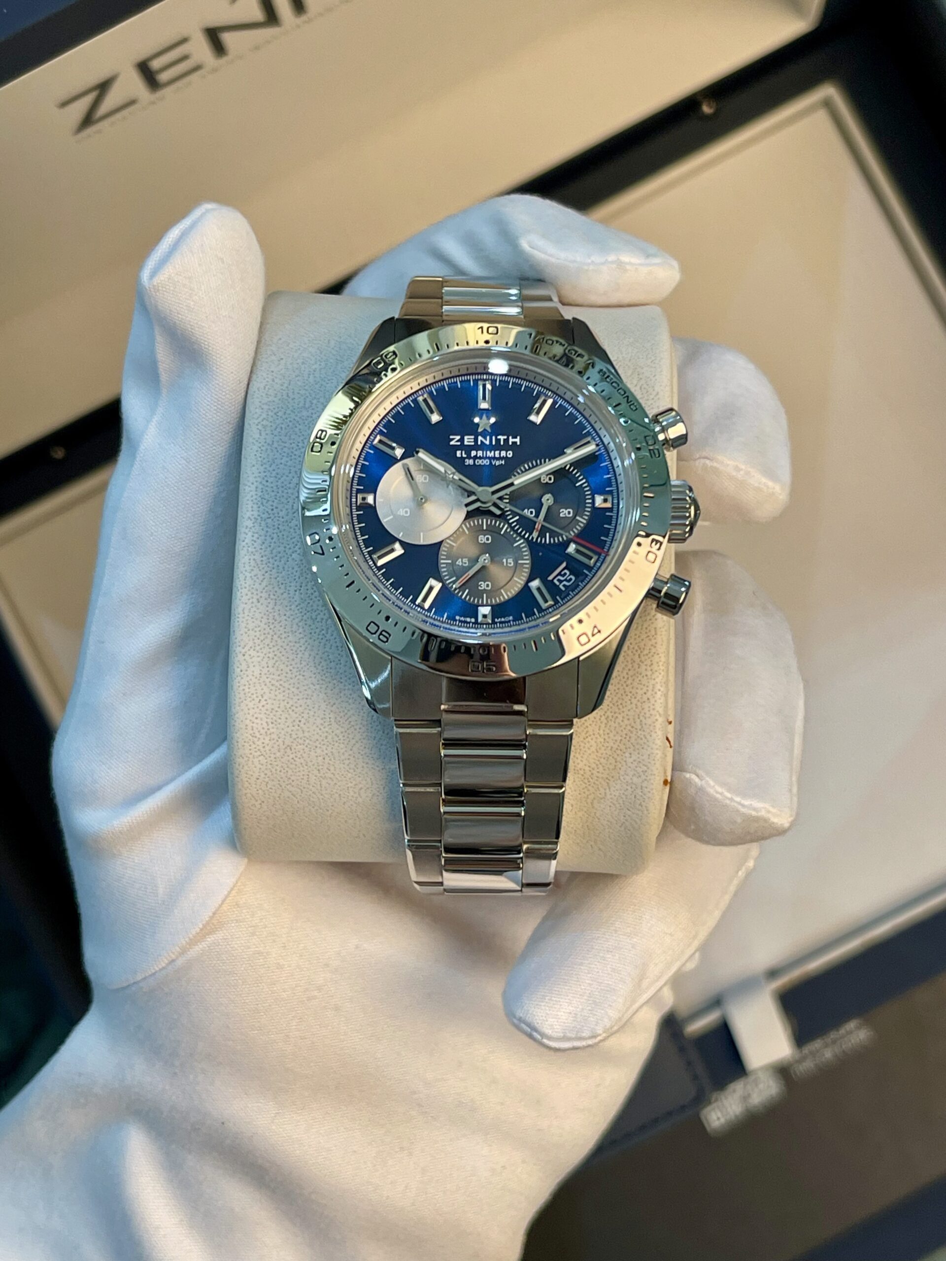 Zenith El Primero wristwatch with blue dial and silver subdials, held in a gloved hand.