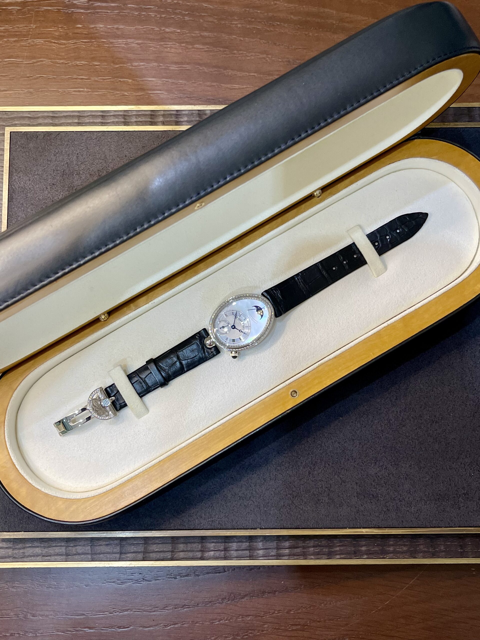 Wristwatch with a black leather strap displayed inside a cream-lined wooden box case.