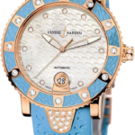 Women’s luxury Ulysse Nardin wristwatch with a blue strap, rose-gold case and diamond-studded bezel, white textured dial, and date window at 6 o'clock.