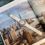 Open magazine showing a city skyline photo with a white wristwatch laid across the pages.