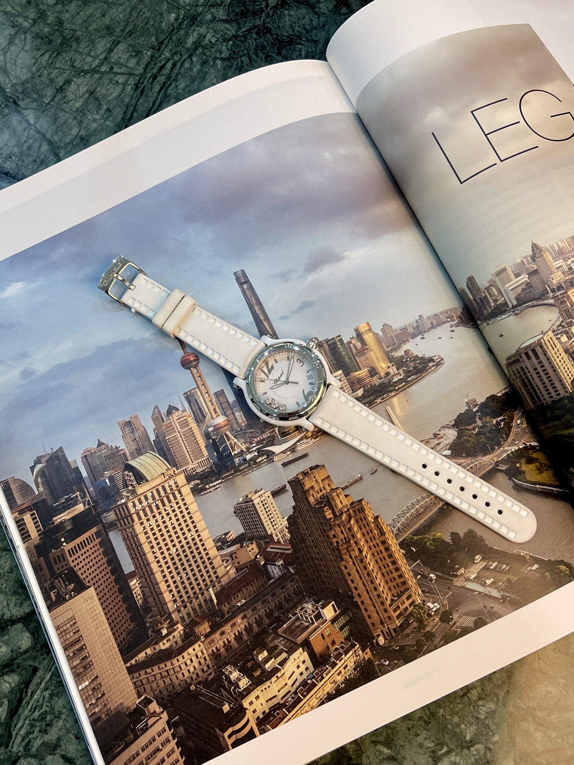 Open magazine showing a city skyline photo with a white wristwatch laid across the pages.