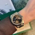 Wrist wearing a Rolex Datejust with a fluted bezel, bronze dial with Roman numerals, and date window at 3 o'clock.
