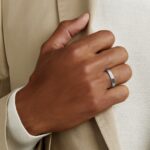 Close-up of a hand with a silver ring adjusting a beige fabric sleeve.