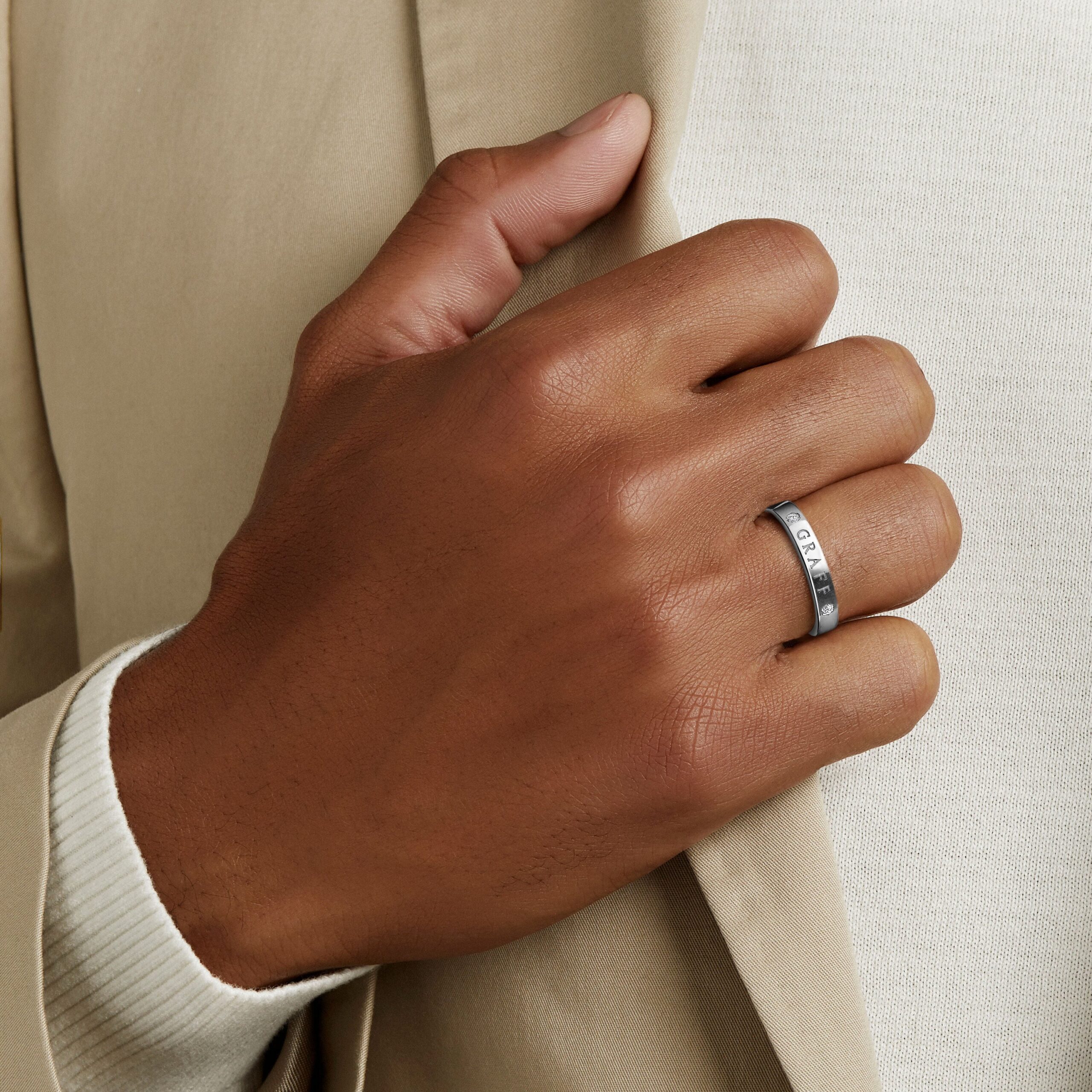 Close-up of a hand with a silver ring adjusting a beige fabric sleeve.