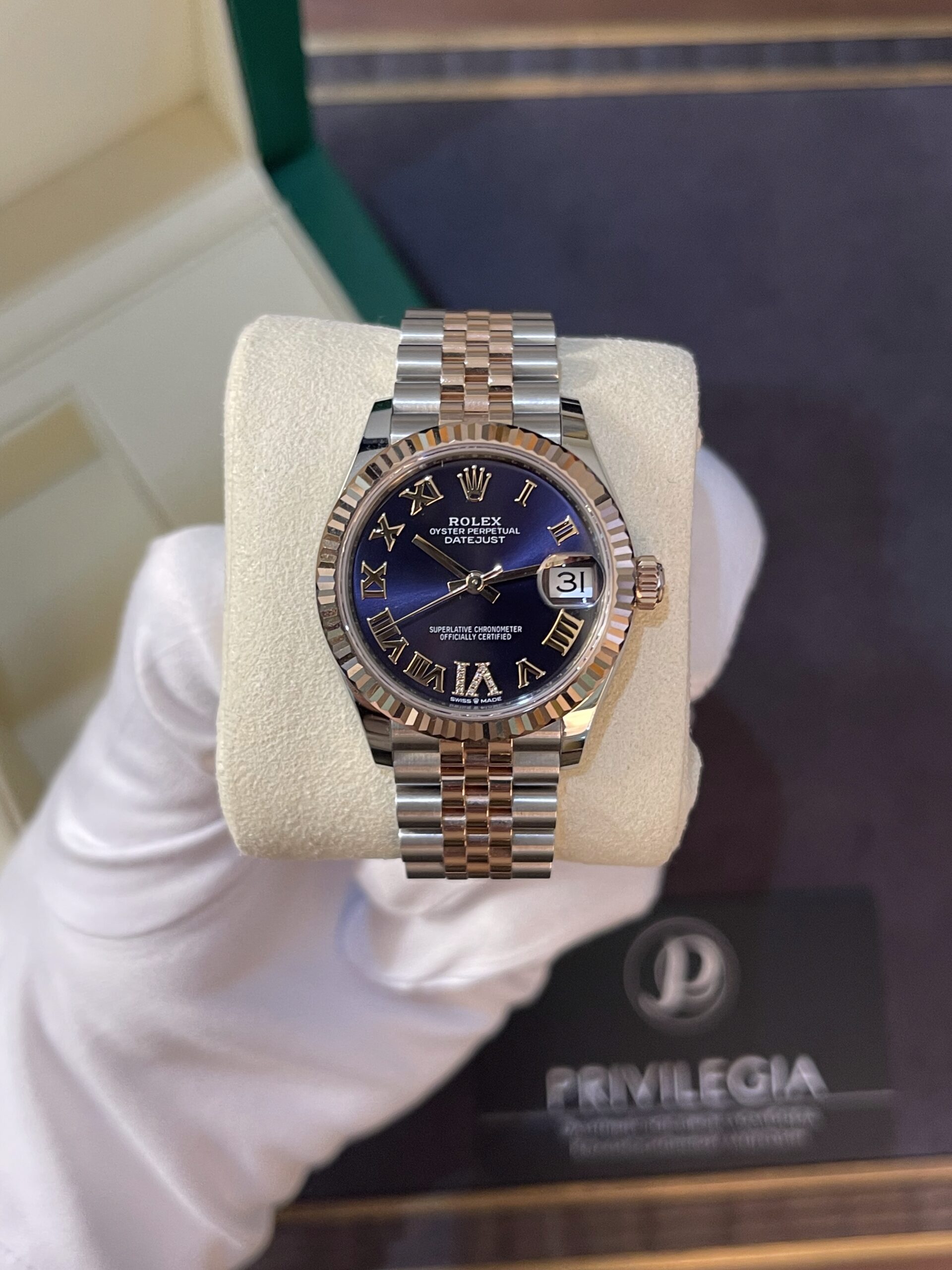 Rolex Datejust wristwatch with a blue dial, Roman numeral markers, and a two-tone silver-and-rose-gold bracelet on a display pillow.