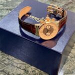 Gold-tone chronograph wristwatch with a brown leather strap resting on a dark blue ULYSSE box, partially showing the brand name and anchor logo.