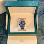 Rolex watch in its green presentation box, with oyster bracelet visible and Rolex logo on the inner box lid