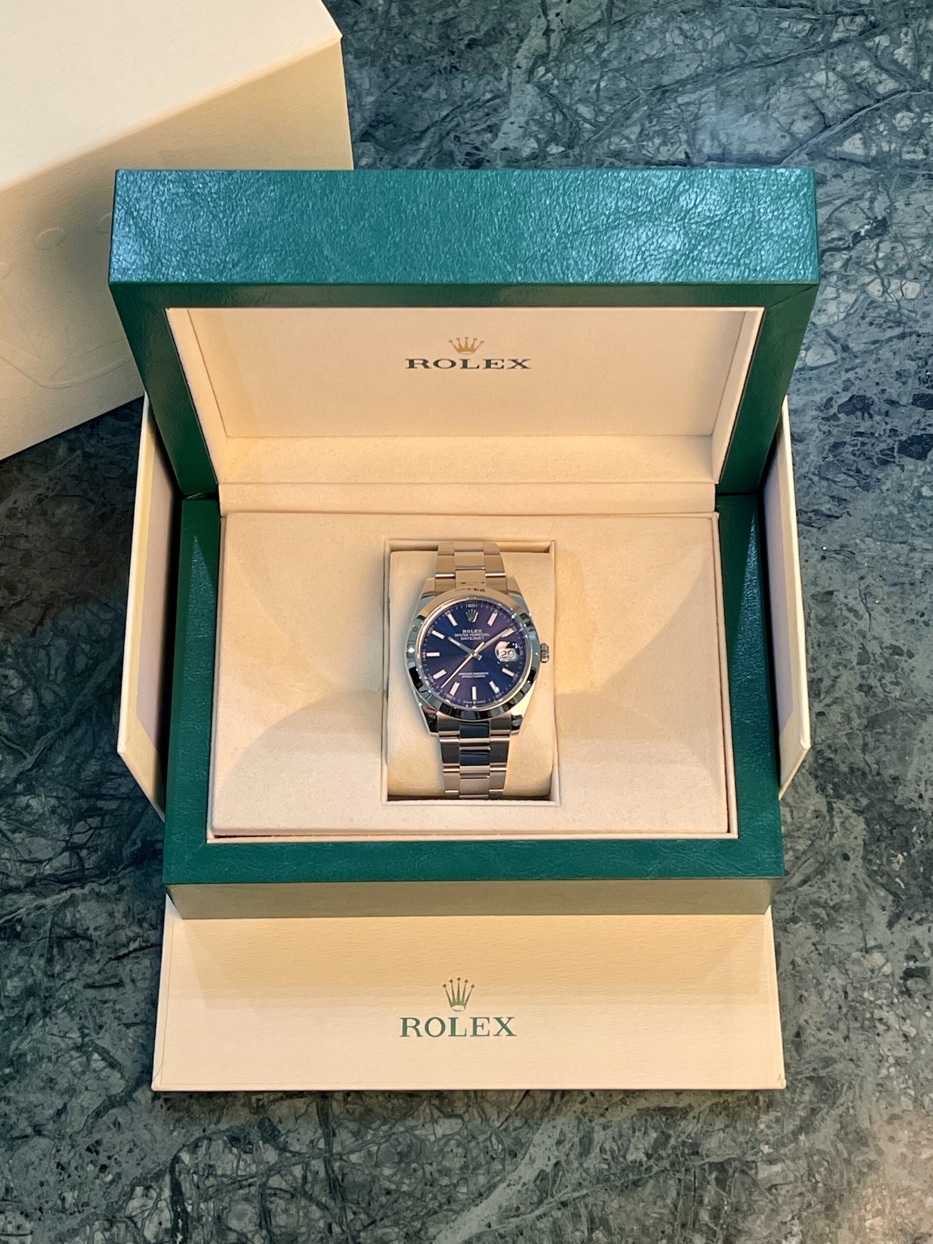 Rolex watch in its green presentation box, with oyster bracelet visible and Rolex logo on the inner box lid