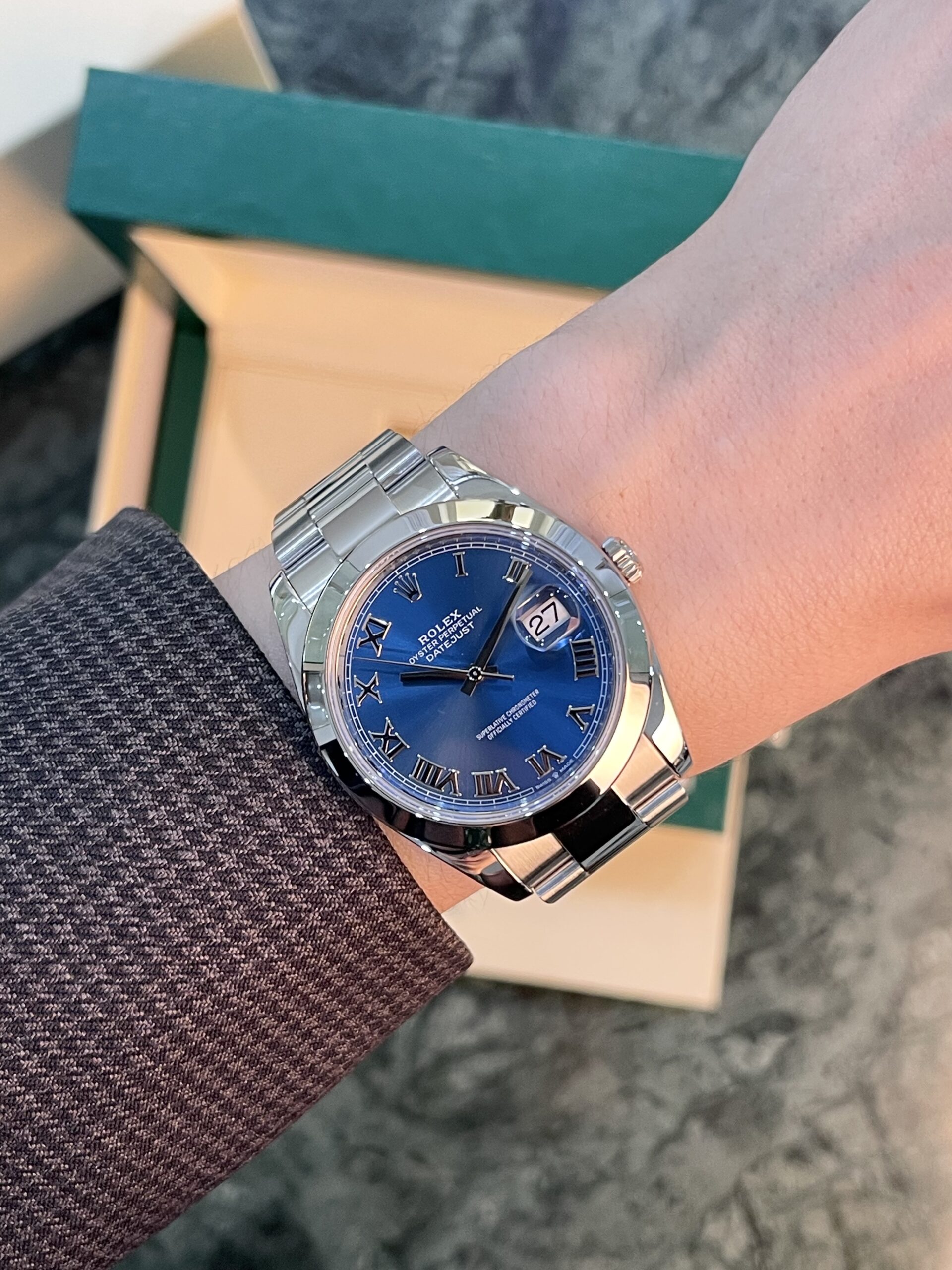 Wristwatch with a blue dial and silver metal band on a forearm, with a green box in the background.