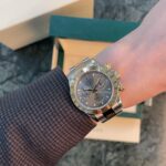 Two-tone Rolex watch on a wrist with a denim sleeve and beige packaging boxes in the background.