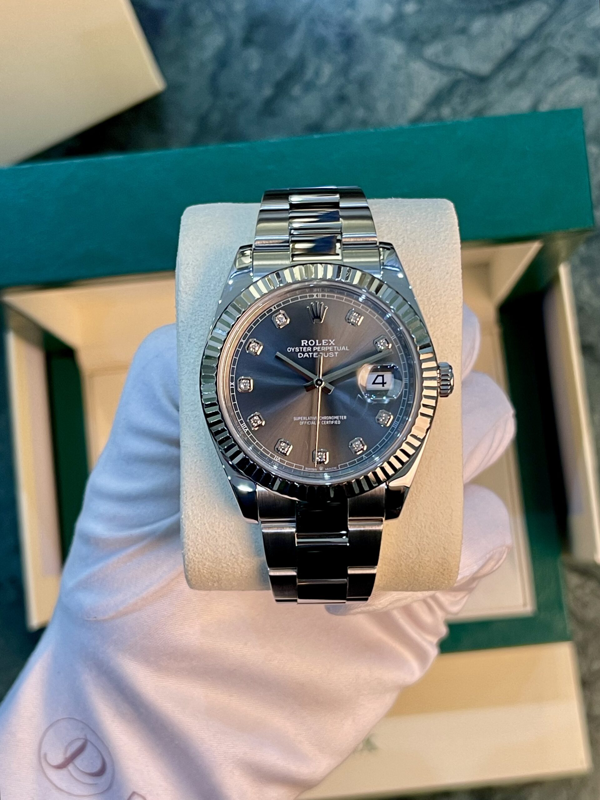 Rolex Oyster Perpetual Datejust watch with a fluted bezel and diamond hour markers on a cushion in a presentation box
