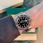 Wristwatch: stainless Rolex GMT‑Master II with brown/black bezel and black dial, date at 3, silver bracelet.