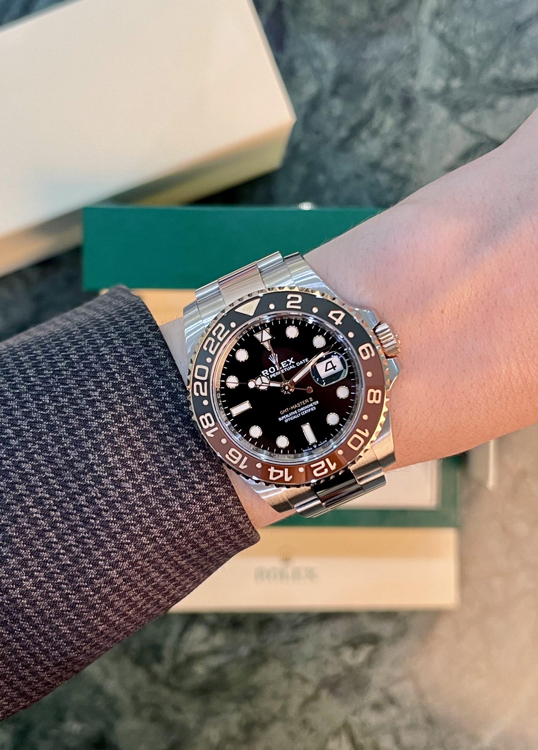 Wristwatch: stainless Rolex GMT‑Master II with brown/black bezel and black dial, date at 3, silver bracelet.
