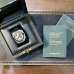 Wristwatch in black presentation box with green warranty booklets on a wooden surface