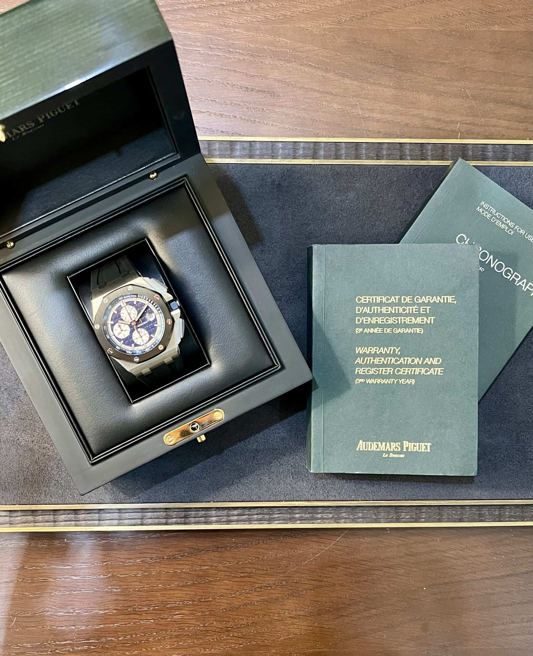 Wristwatch in black presentation box with green warranty booklets on a wooden surface