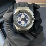A luxury stainless steel chronograph watch with a blue patterned dial held by a gloved hand.