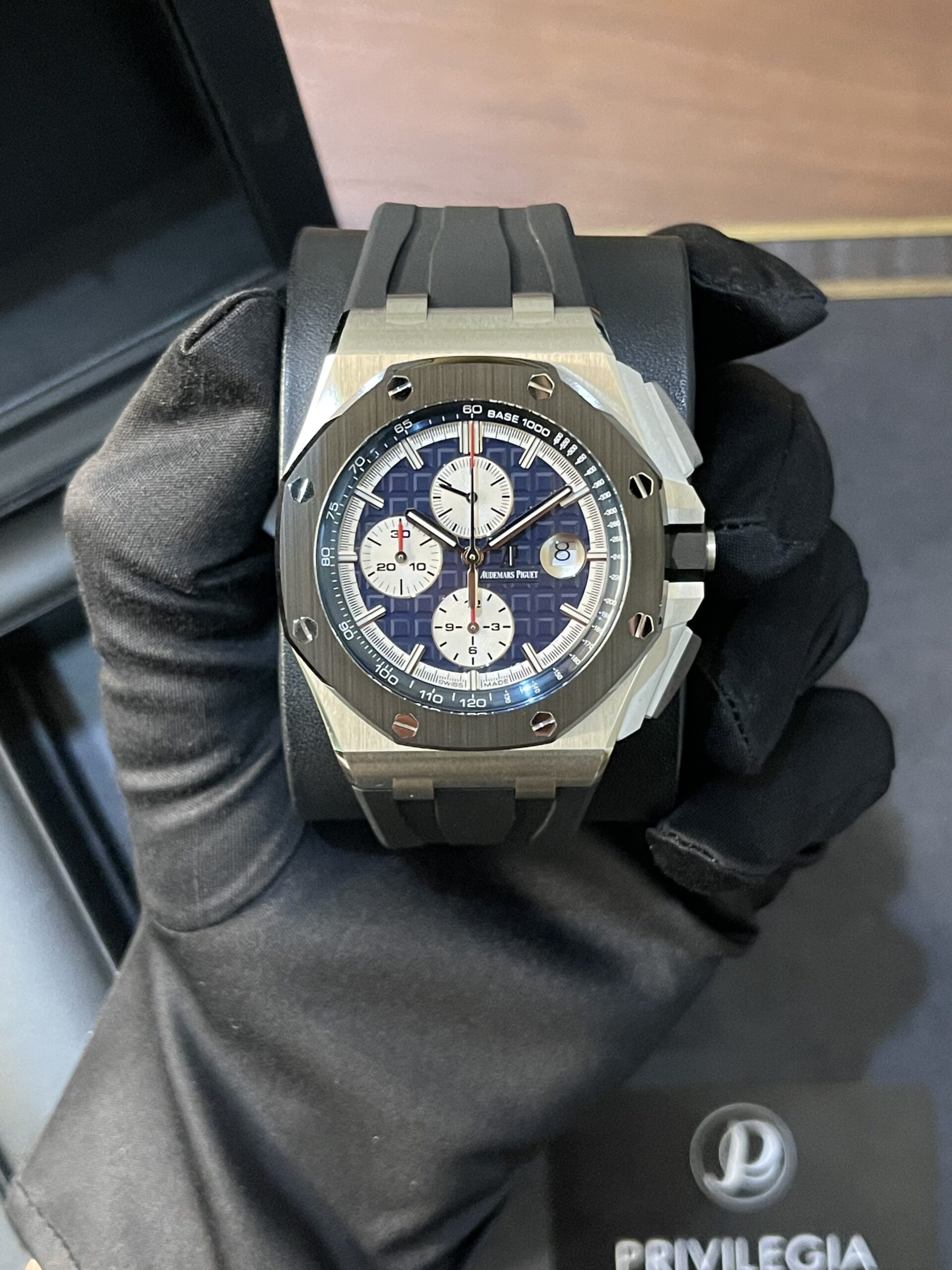 A luxury stainless steel chronograph watch with a blue patterned dial held by a gloved hand.