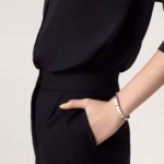 Close-up of a person in a black outfit with a hand in their pocket and a silver bracelet on the wrist.