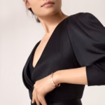 Close-up of a woman in a black V-neck dress with draped shoulders, wearing a rose-gold bracelet on her wrist