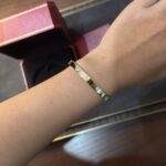 Gold bracelet with small crystal-like stones on a wrist, pink jewelry box in the background.