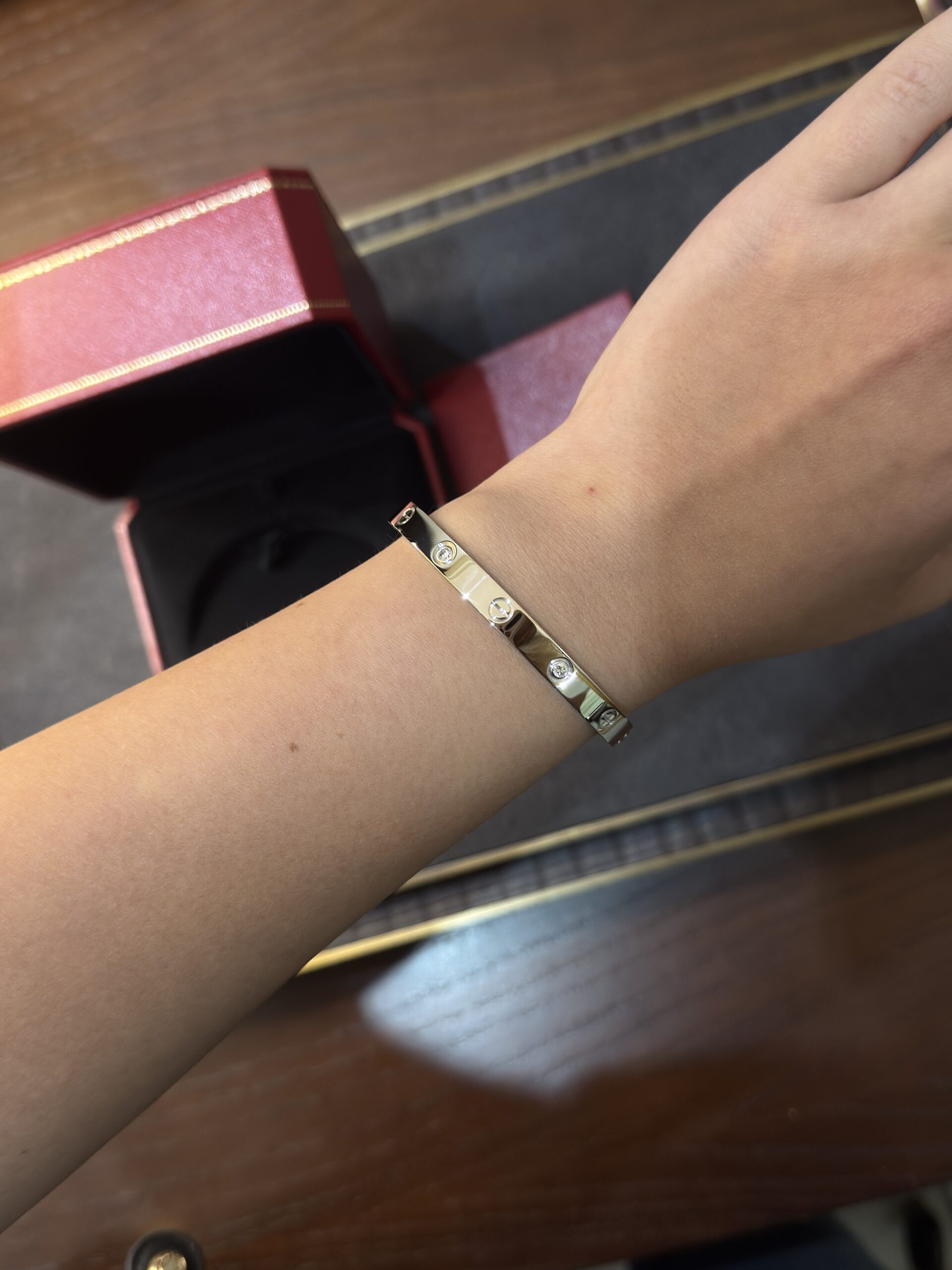 Gold bracelet with small crystal-like stones on a wrist, pink jewelry box in the background.