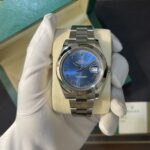 Rolex Datejust watch with blue dial and Roman numeral markers in a green presentation box held by gloved hand