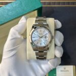 Silver Rolex Datejust wristwatch with a metal bracelet displayed on a cream cushion inside an open green Rolex box, held by gloved hand