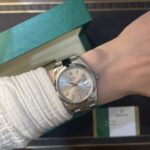 Silver Rolex Datejust watch on the wrist, with a green Rolex box in the background
