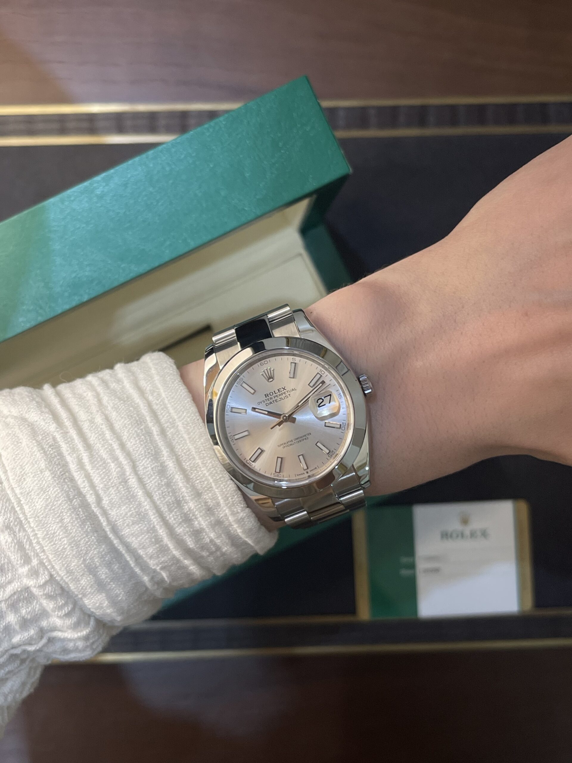 Silver Rolex Datejust watch on the wrist, with a green Rolex box in the background