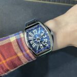 Wristwatch with a blue-framed, bold-dial Franck Muller Yachting on a red plaid sleeve.