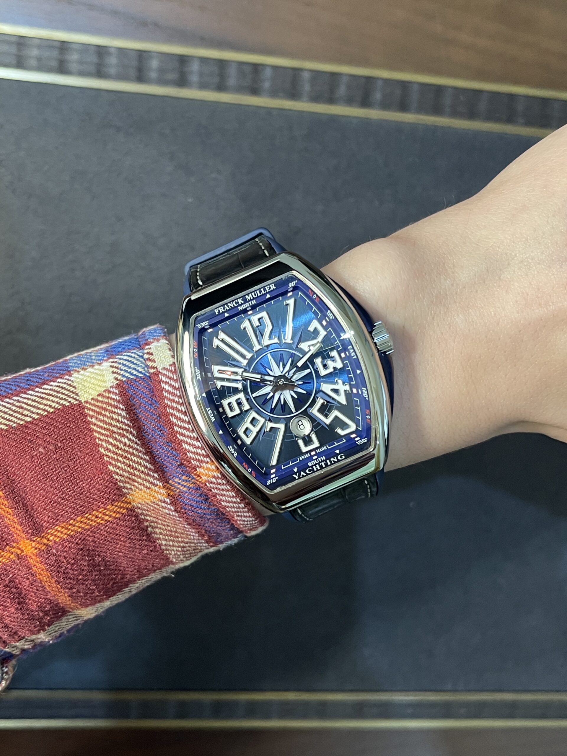 Wristwatch with a blue-framed, bold-dial Franck Muller Yachting on a red plaid sleeve.