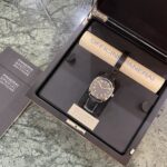 Panerai watch in an open presentation box with a black dial and gold case, brown leather strap, beside Panerai edition booklets.
