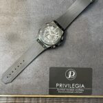 Skeleton-dial wristwatch with a gray ribbed strap laid on a gray surface next to a Privilege-branded card.