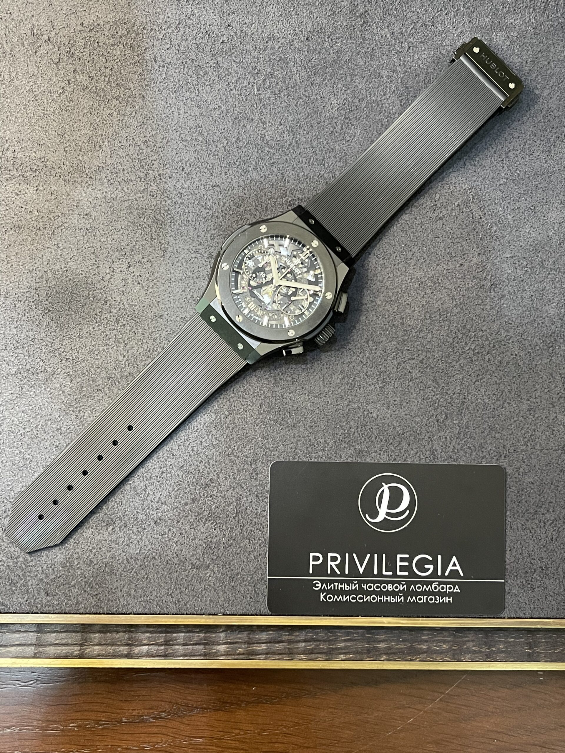 Skeleton-dial wristwatch with a gray ribbed strap laid on a gray surface next to a Privilege-branded card.