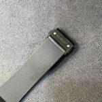 Close-up of a black metal watch band with Hublot clasp against a gray carpet.