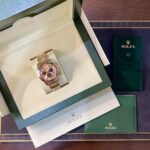 Rose gold Rolex watch in an open green presentation box with cream interior and matching green paperwork pouches nearby.