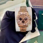 Rose gold Rolex Cosmograph Daytona watch on a foam cushion inside a green box, held by a gloved hand.