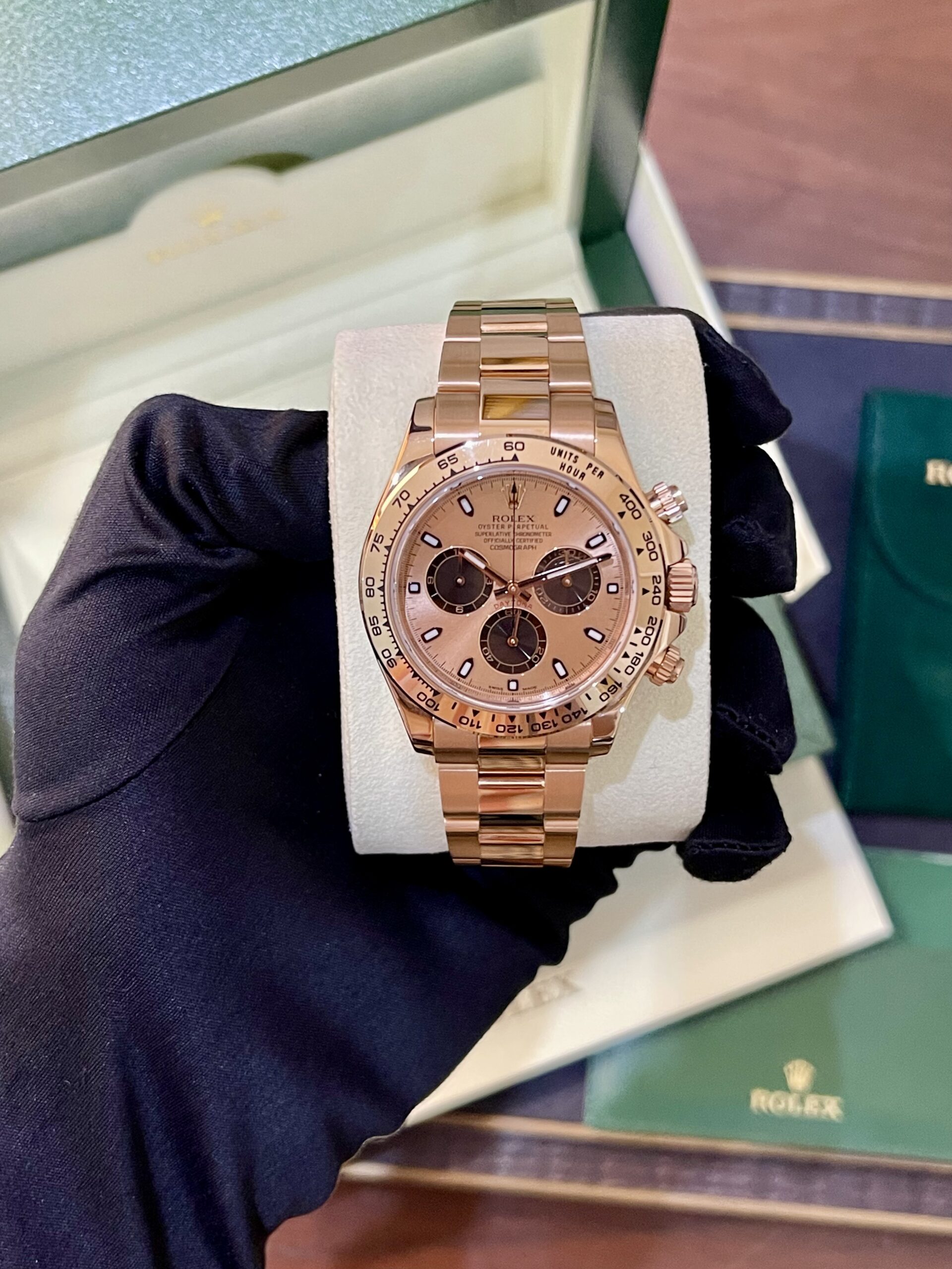 Rose gold Rolex Cosmograph Daytona watch on a foam cushion inside a green box, held by a gloved hand.