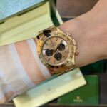 Gold Rolex chronograph on a striped shirt cuff, with a green box in the background.