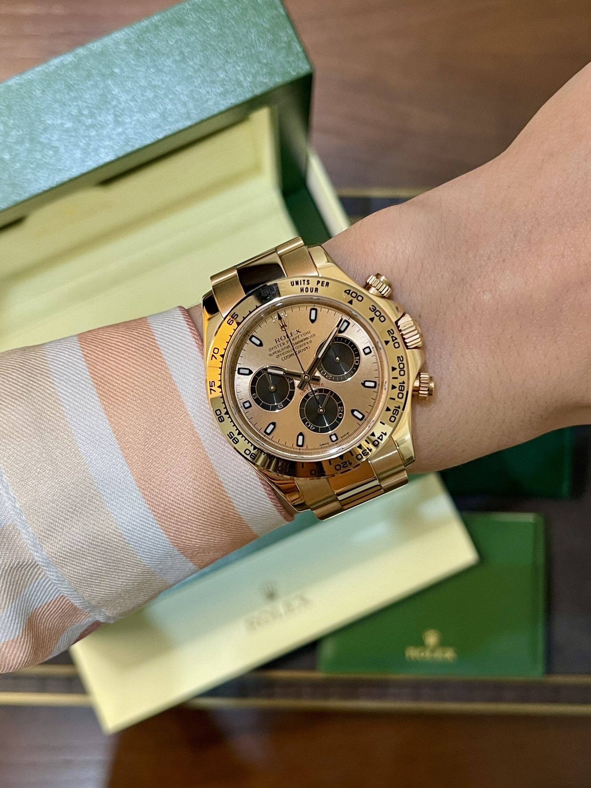 Gold Rolex chronograph on a striped shirt cuff, with a green box in the background.
