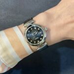 Wristwatch with a blue dial and diamond hour markers on a striped orange and white shirt cuff.