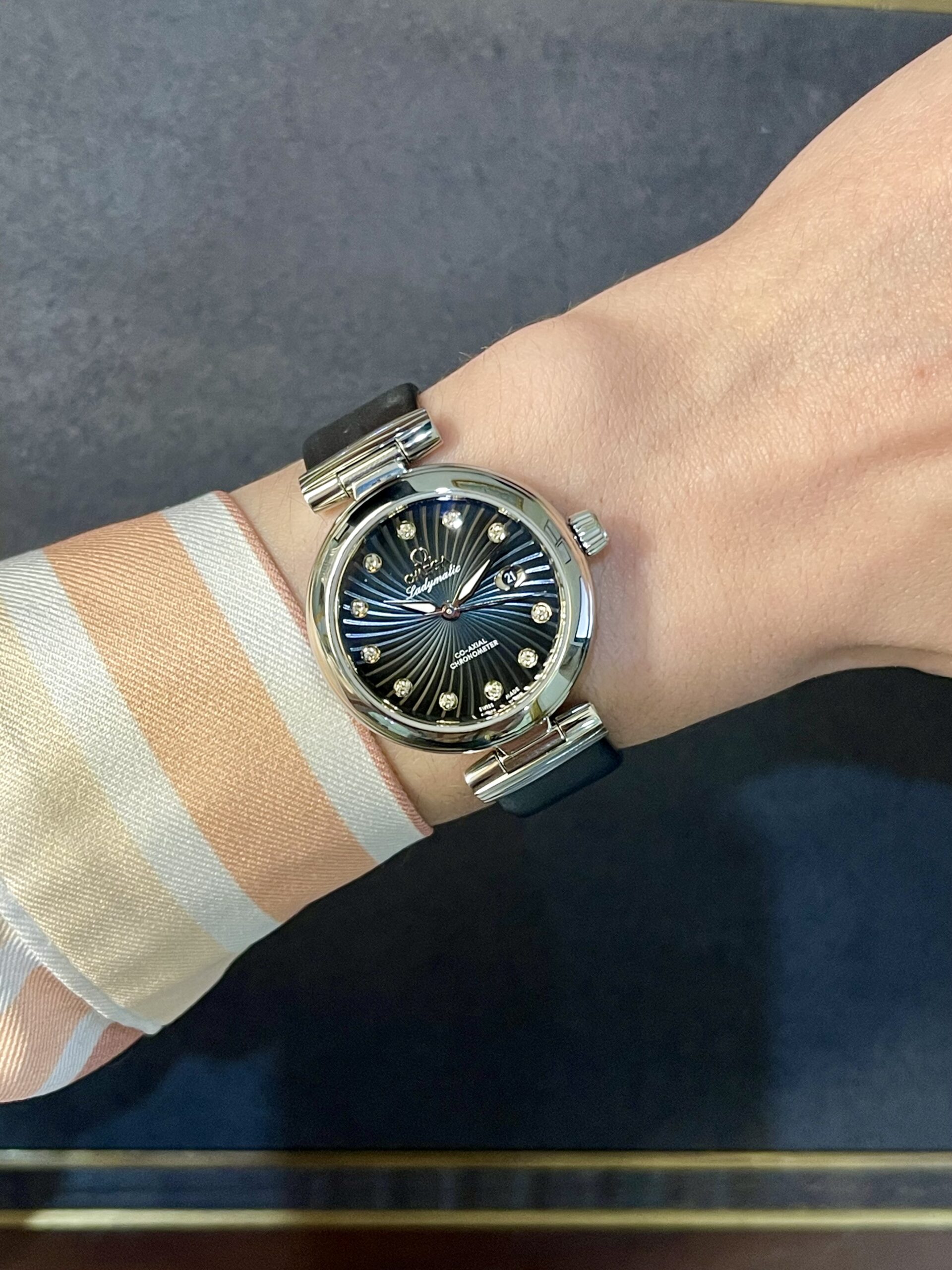 Wristwatch with a blue dial and diamond hour markers on a striped orange and white shirt cuff.